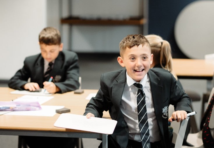 A student in a classroom holding a whiteboard and smiling.