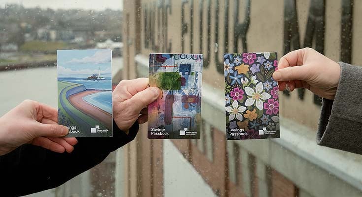 Three hands holding Newcastle Building Society passkbooks, with bespoke artwork designs. 