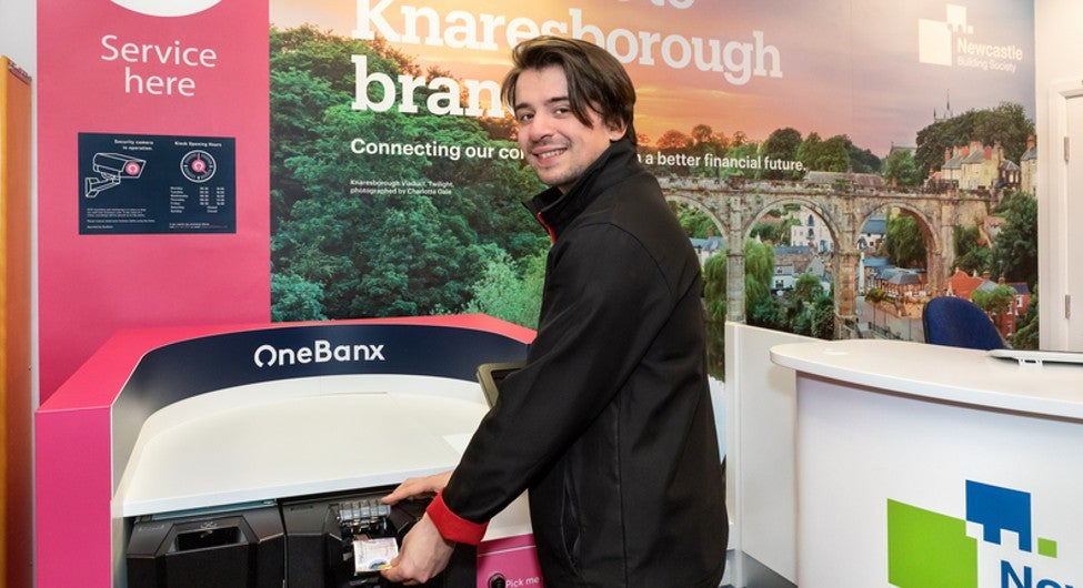 A man using a OneBanx kiosk to deposit cash inside the Newcastle Building Society Knaresborough branch.