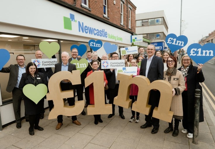 A group of people outside of a Newcastle Building Society branch holding up signs that say "£1m".