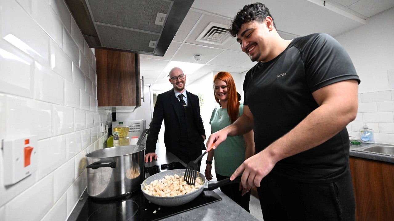 A group of people stood cooking and chatting in a kitchen.