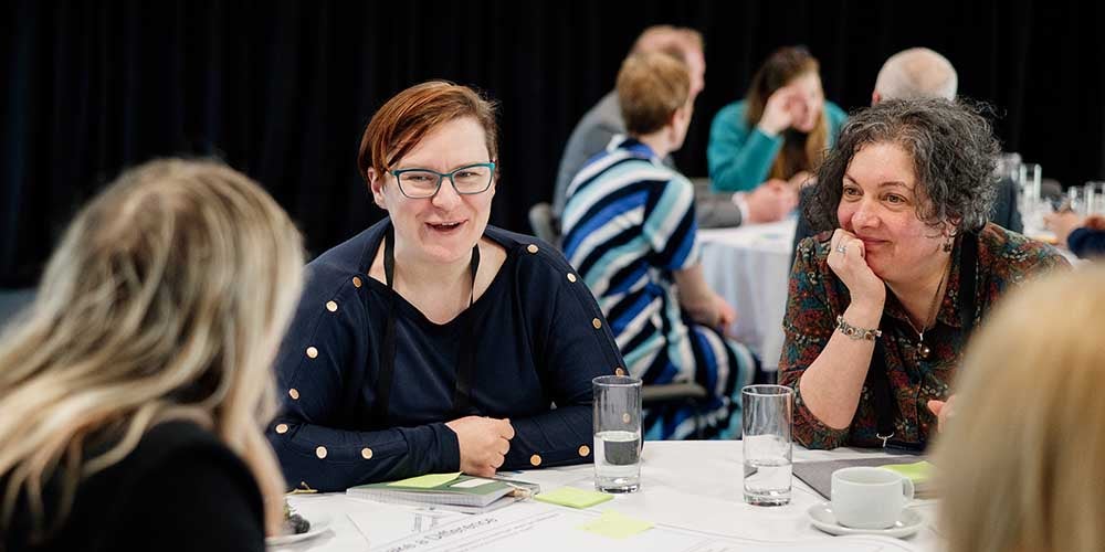 Three woman sat at a table talking to each other. 