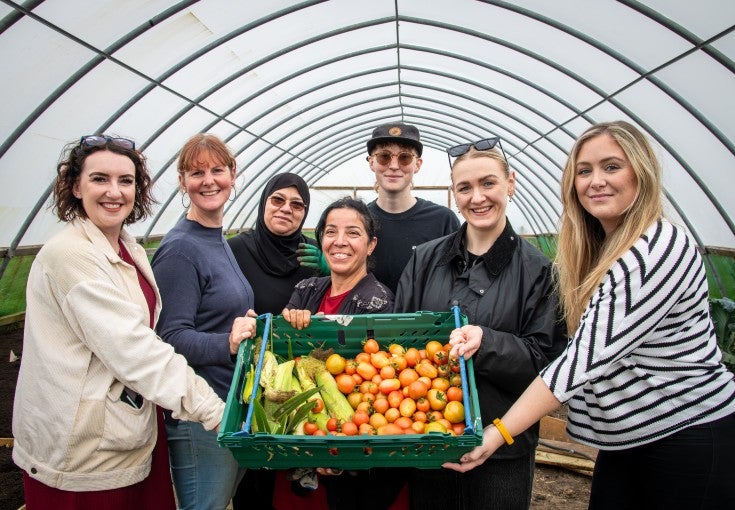 A group of Newcastle Building Society colleagues and members of West End Women and Girls Centre stood holding a basket of vegetables. The vegetables have been grown by members of the charity on their farm.