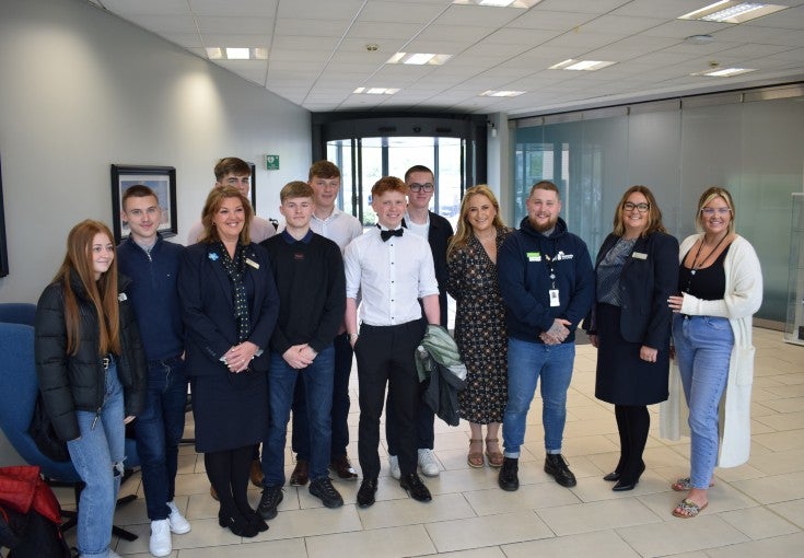 A group of students and office workers posing for a photo in the main reception of an office. 