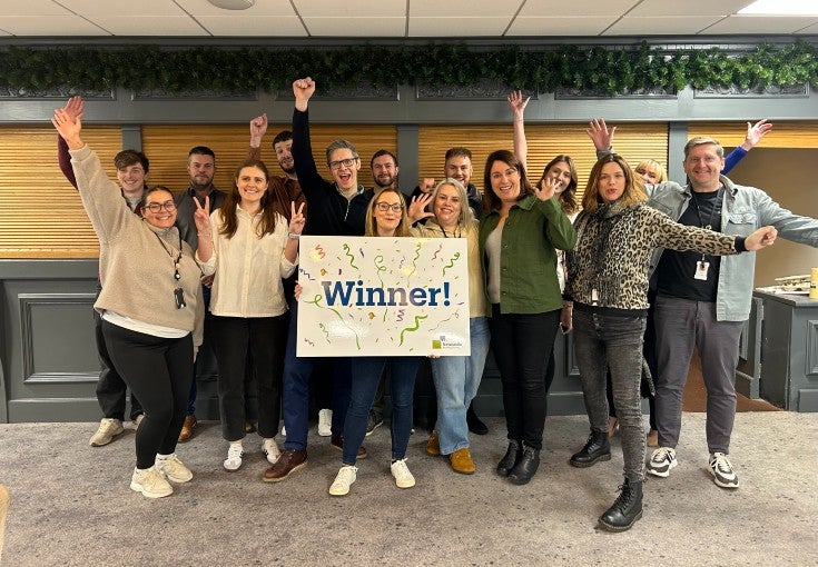 A group of Newcastle Building Society waving their arms in the air and stood behind a sign that says "Winner!"