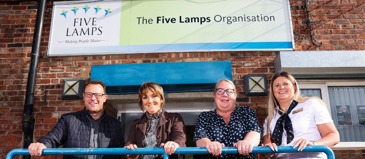 A group of people stood outside The Five Lamps Organisation, holding onto the railing in front of them 