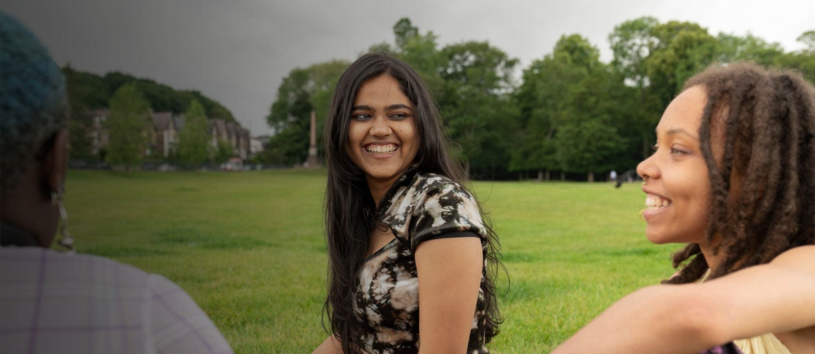 A young adult girl with her friends sat in a park smiling. 