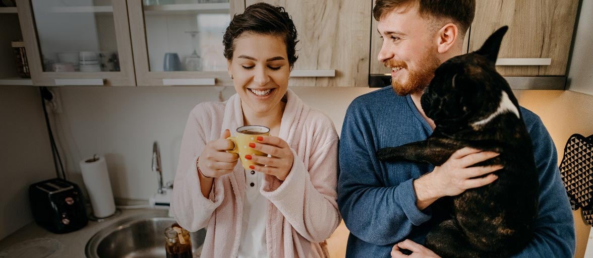A couple stood in their kitchen with their dog and a cup of coffee