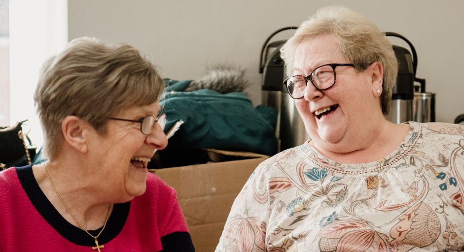 Two elderly ladies laughing with each other as they play bingo.