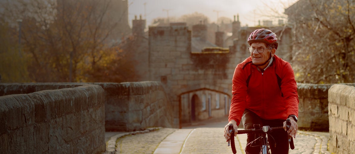 Man wearing a red jacket riding a bicycle in a historic medieval village. 