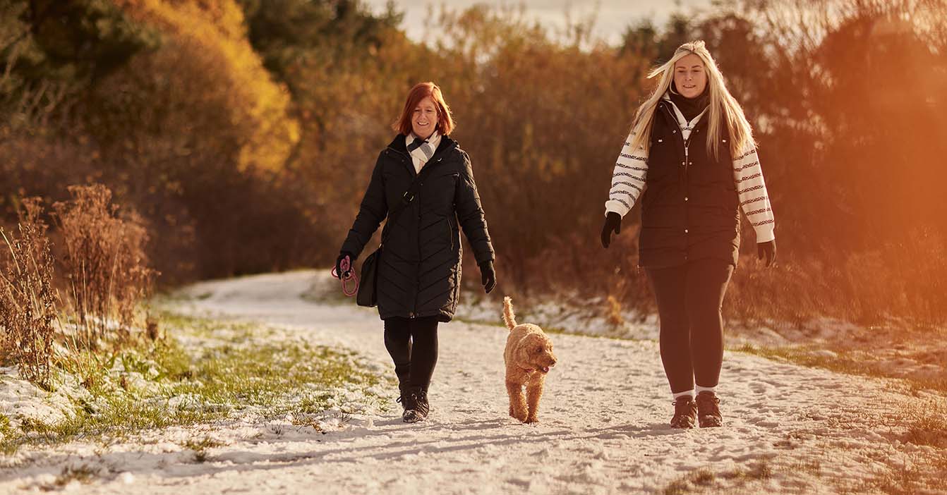 To women walking the the snow with their dog. 