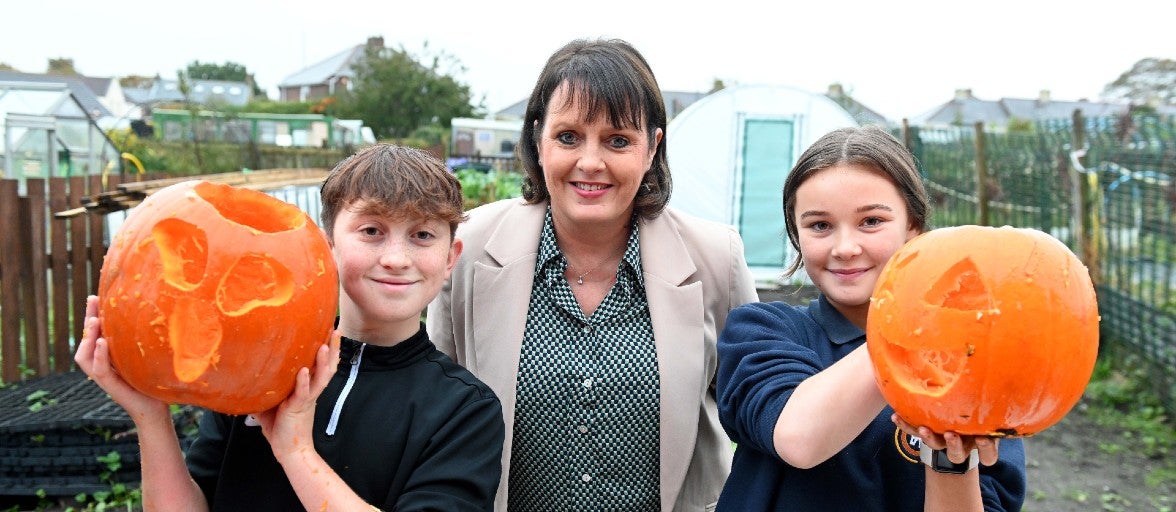 A boy and girl stood holding a carved pumpkin on either side of our Head of Mortgage Service Centre, Sue Scott.