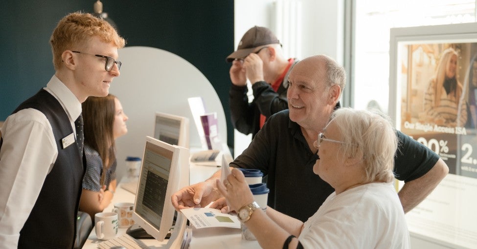 A Newcastle Building Society Customer Adviser speaking to two customers.