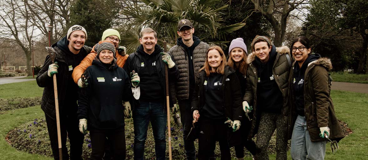 Group of Newcastle Building Society colleagues stood in Wallsend park with gardening tools in hand smiling