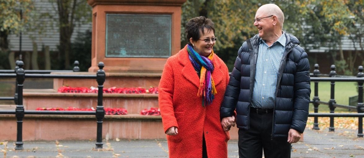 A middle aged couple hold hands by a memorial in Gosforth