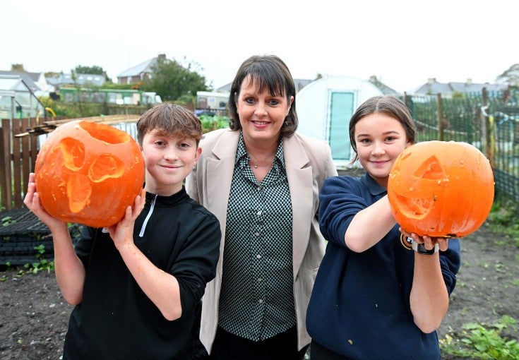 A boy and girl stood holding a carved pumpkin on either side of our Head of Mortgage Service Centre, Sue Scott.