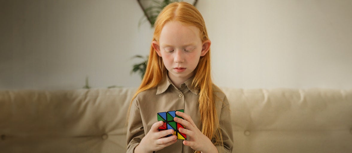 A young girl sits on a sofa and plays with a rubix cube.