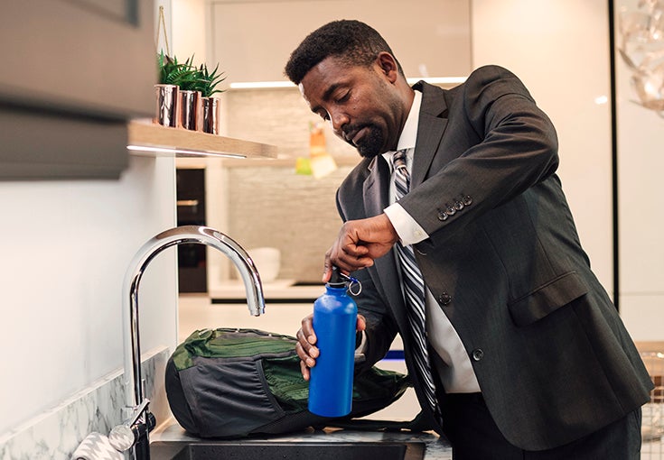 A father fills up his water bottle in the family home before work.