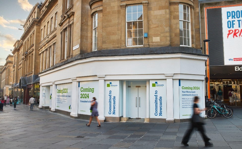 Exterior of the upcoming new Newcastle Building Society Monument branch. The windows are covered in large white signs that read "Coming 2024" in green font. 