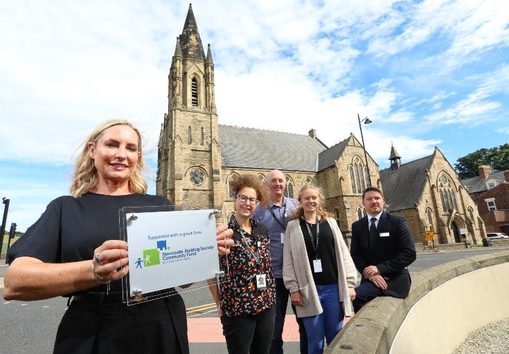A group of people in front of a church in Sunderland with a community grant plaque.