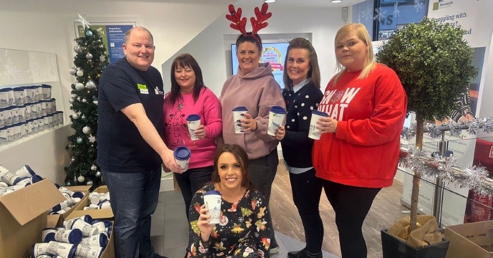 A group of Newcastle Building Society colleagues posing with reusable coffee mugs inside their branch and surrounded by them as well.
