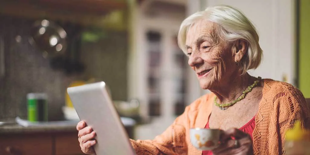 Elderly woman shopping online with her tablet device while drinking a cup of tea