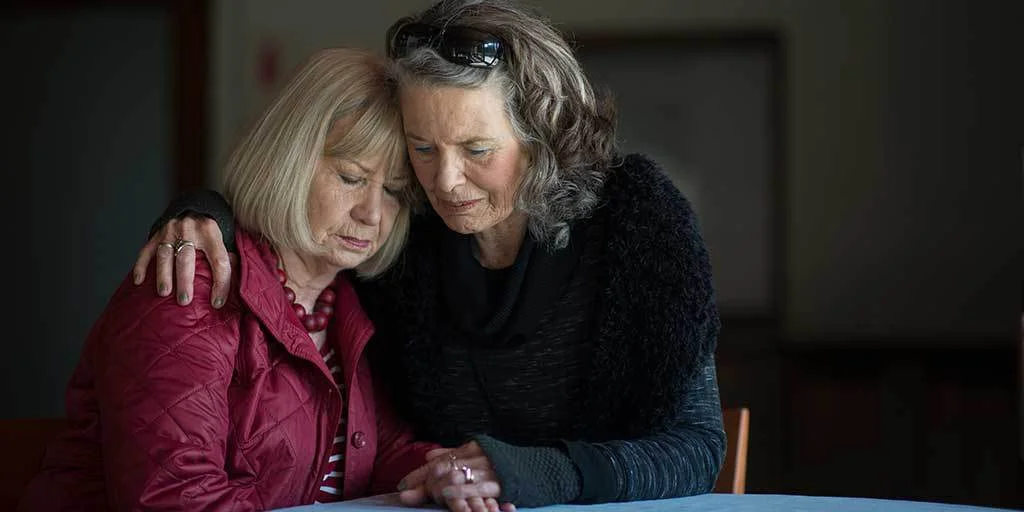 Two elderly woman holding each other as they grieve a loved one's death