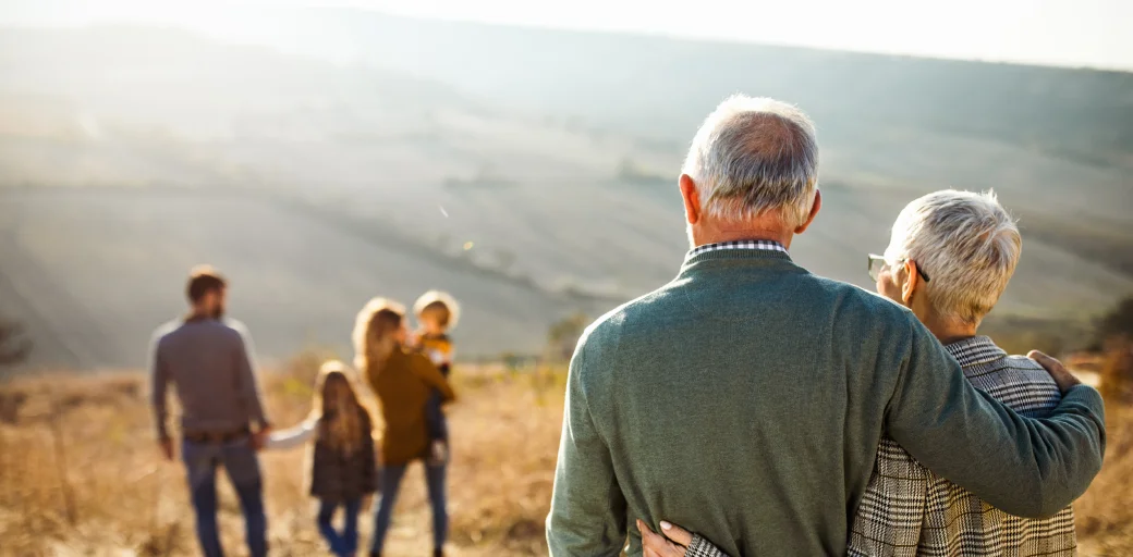 Elderly couple holding one another as they watch their family walk in front of them in distance