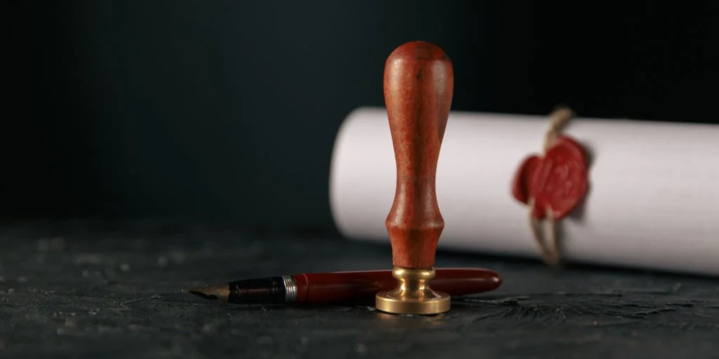 Classical stamp sitting in front of an old fountain pen with scroll behind it