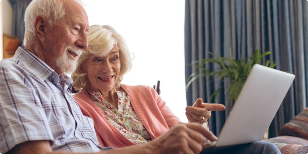 Elderly couple smiling as they use a laptop
