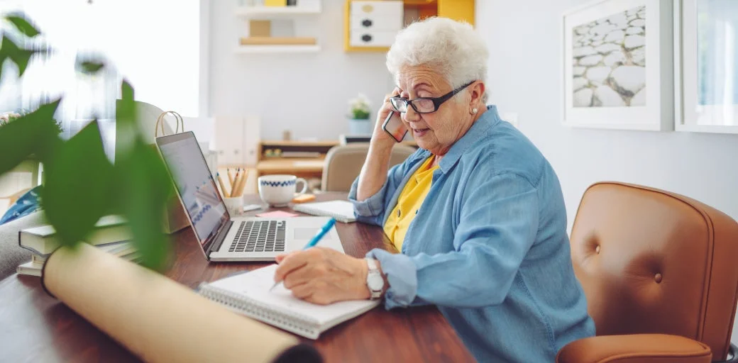 Elderly woman using mobile phone and laptop as she works at home