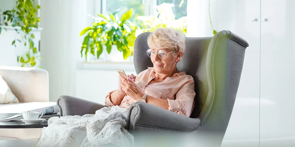 Elderly woman on her mobile phone with a blanket over her knees and a cup of tea on the side table