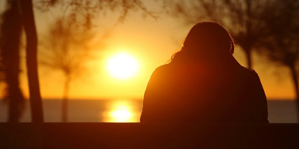 Silhouette of a woman sitting on a park beach whilst looking upon a sunset
