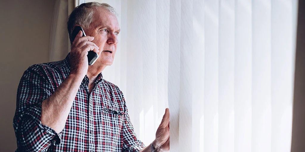 Man worryingly looking out his window as he is on the phone with emergency services