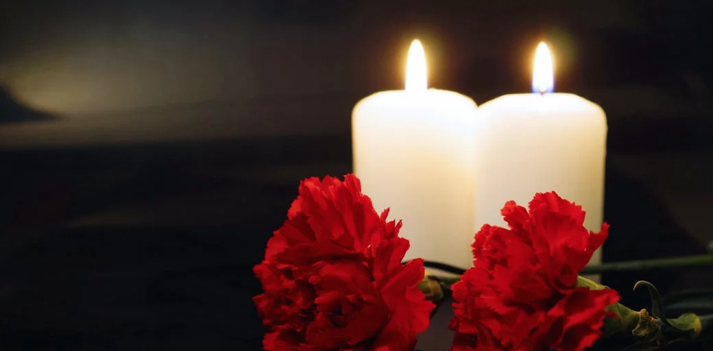 Two rose flowers laying in front of two light candles