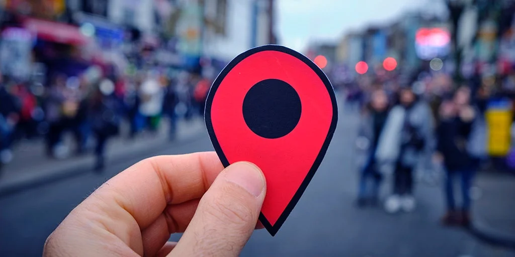 Close up of a red location marker in front of blurred busy street