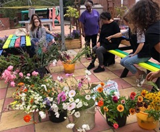 People sitting on coloured benches looking at buckets of flowers