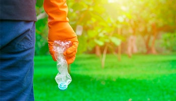 Close up of someone standing in a garden wearing gloves and holding a plastic water bottle