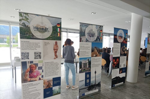 Einblick in die Wanderausstellung „Heimat – regionale Identität in Europa“ mit Publikum im Hintergrund bei der Ausstellungseröffnung am 05.05.2025 im Oberschulzentrum Mals. Foto: FS Tisens. Einblick in die Wanderausstellung „Heimat – regionale Identität in Europa“ mit Publikum im Hintergrund bei der Ausstellungseröffnung am 05.05.2025 im Oberschulzentrum Mals. Foto: FS Tisens.