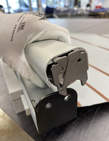 A gloved hand holds a roller coupler featuring Lufthansa's metal 3D-printed titanium latch.