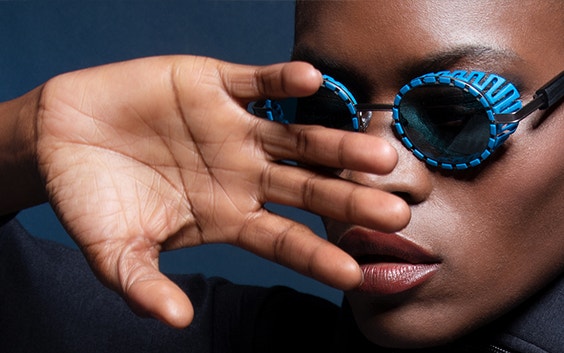 Mannequin féminin noir posant avec sa main devant son visage et portant des lunettes de soleil bleues de la collection JFRey Nautinew