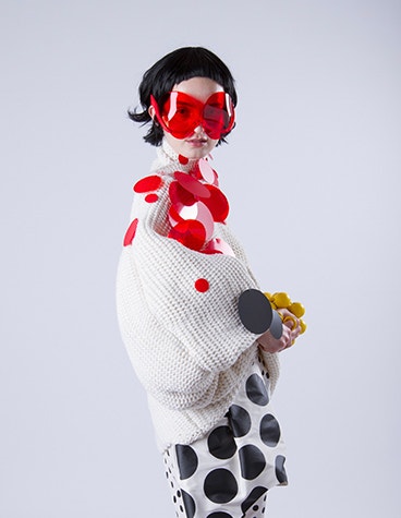 Model wearing a white outfit with red and black circles and red sunglasses designed by David Ring