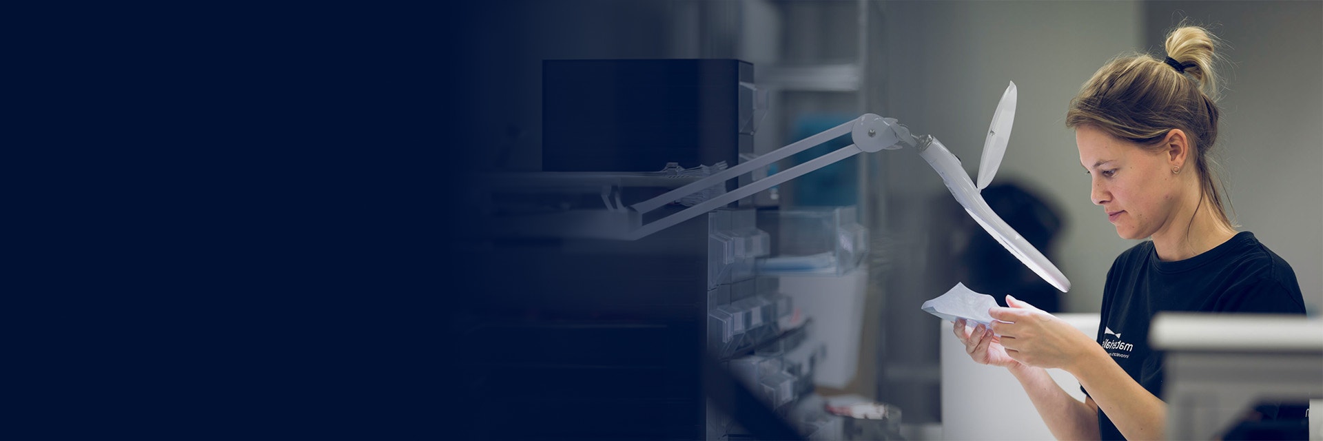 Woman inspecting a part under a magnifying glass in the Materialise production area