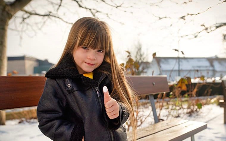 Young girl posing by a bunch, giving a thumbs up, with white paint on her finger