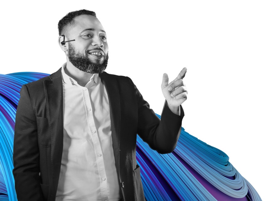 Man in a suit, pointing and smiling while wearing a headset, in black and white. The Mimics Innovation Suite signature blue and purple swirl is behind him