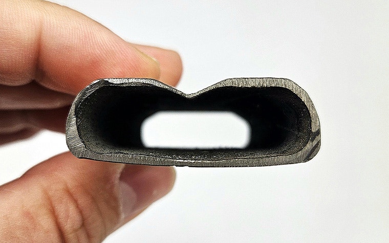 A close-up of a hand holding one half of Alugear's titanium 3D-printed crank arm, cut in half to show the hollow interior and thin walls.