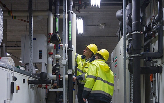 Two workers in safety gear inspecting pipes and machinery