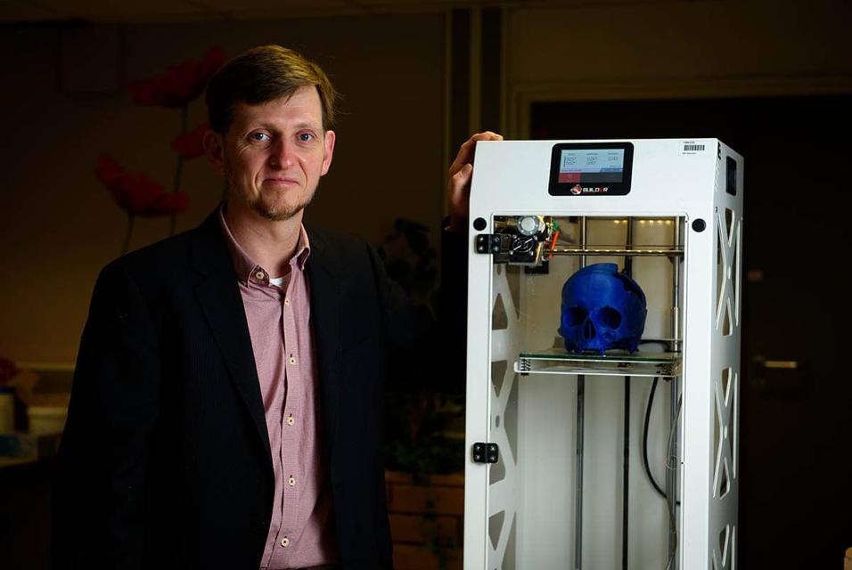 Man standing next to a 3D printer 3D printing a skull model