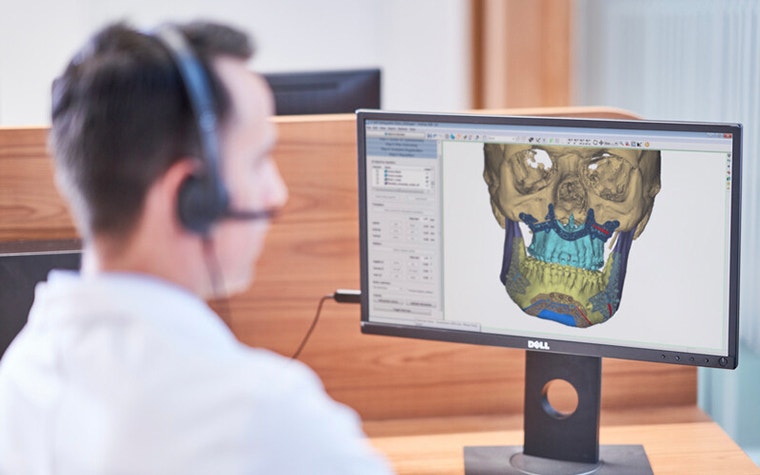 A clinical engineer looks at a 3D software image of human skull on his computer screen while wearing a headset 