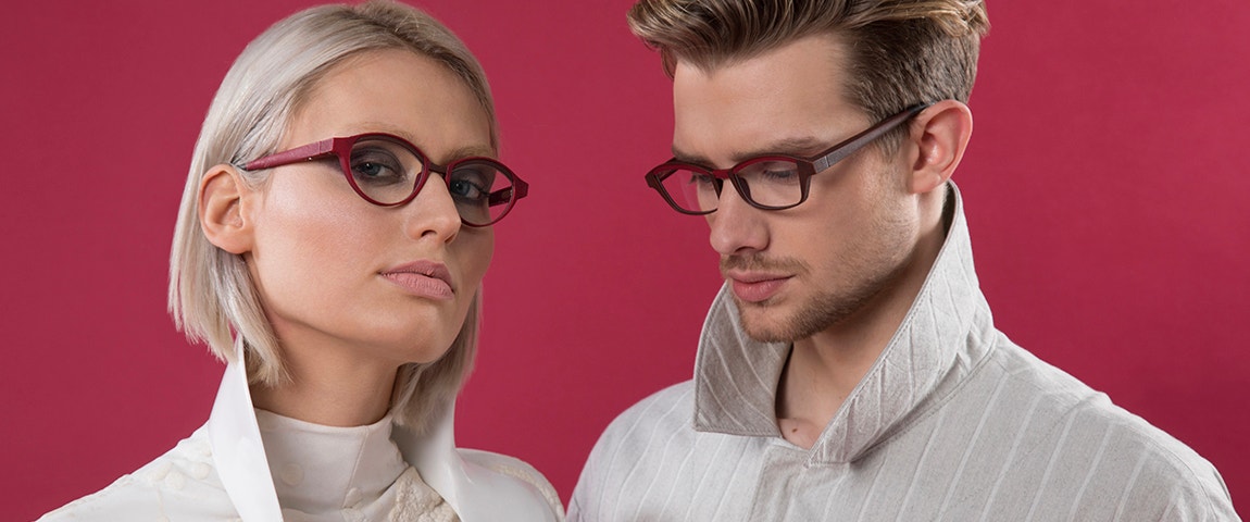 Due modelli davanti a uno sfondo rosso che indossano occhiali dalla montatura rossa della collezione Hoet Cabrio Bi-Color